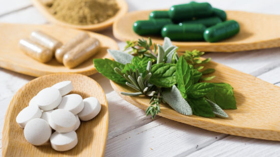 Silencing Doctors on Nutrition COVID herbal leaves, ground herb powder and medicament pills on bamboo spoons, white wooden table