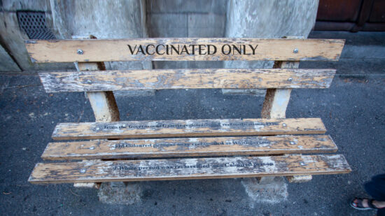 Vaccinated Only For "whites only" - a bench in Cape town. Bench with the inscription, as the memory of apartheid and segregation in South Africa. Memorial bench and feet of a passing boy